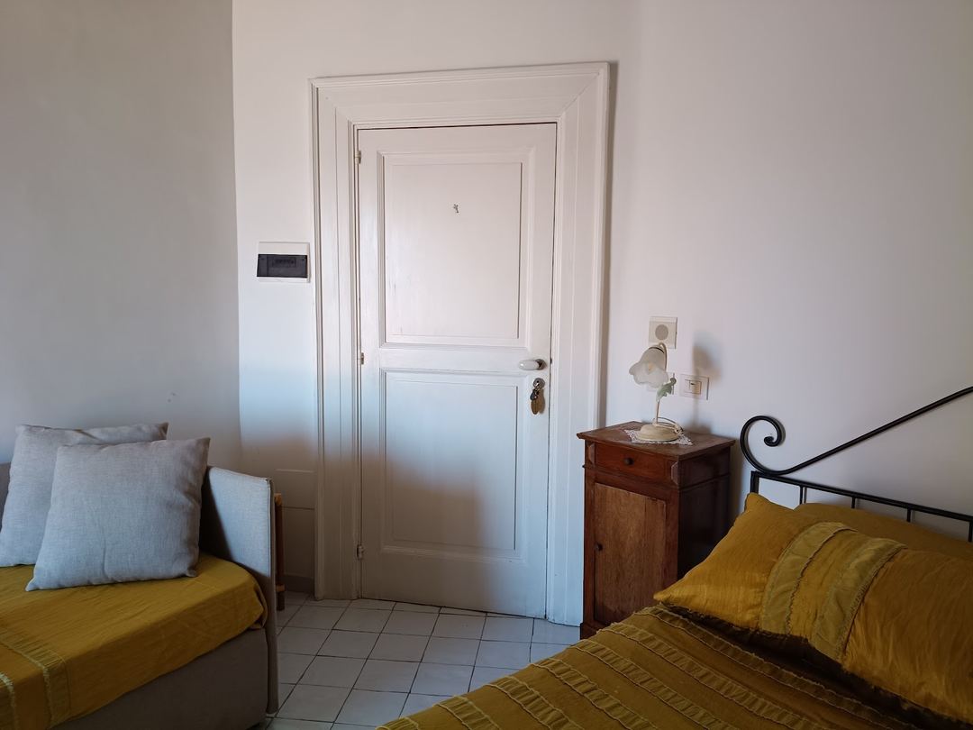 A modest bedroom featuring two single beds with mustard-yellow bedding, a wooden nightstand, and a white paneled door.