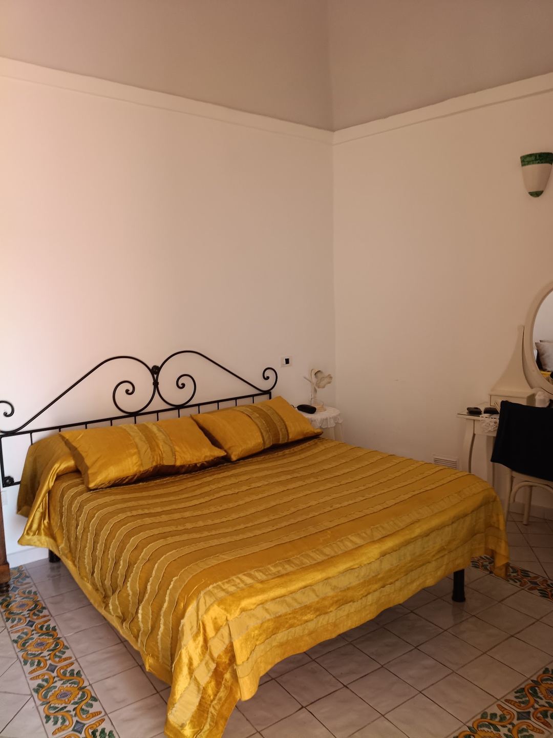 A bedroom with a decorative wrought iron bed frame dressed in golden yellow bedding, featuring a mirror and vanity area.